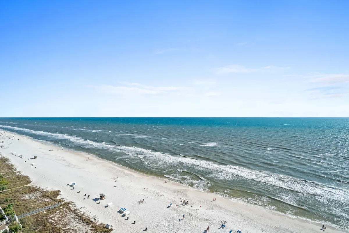 This image captures a vibrant beach scene with gentle ocean waves, sunbathers relaxing in beach chairs, and people enjoying beach games and walks along the shore. The sky suggests a relaxed, sunlit atmosphere perfect for active escapes and seaside adventures.
