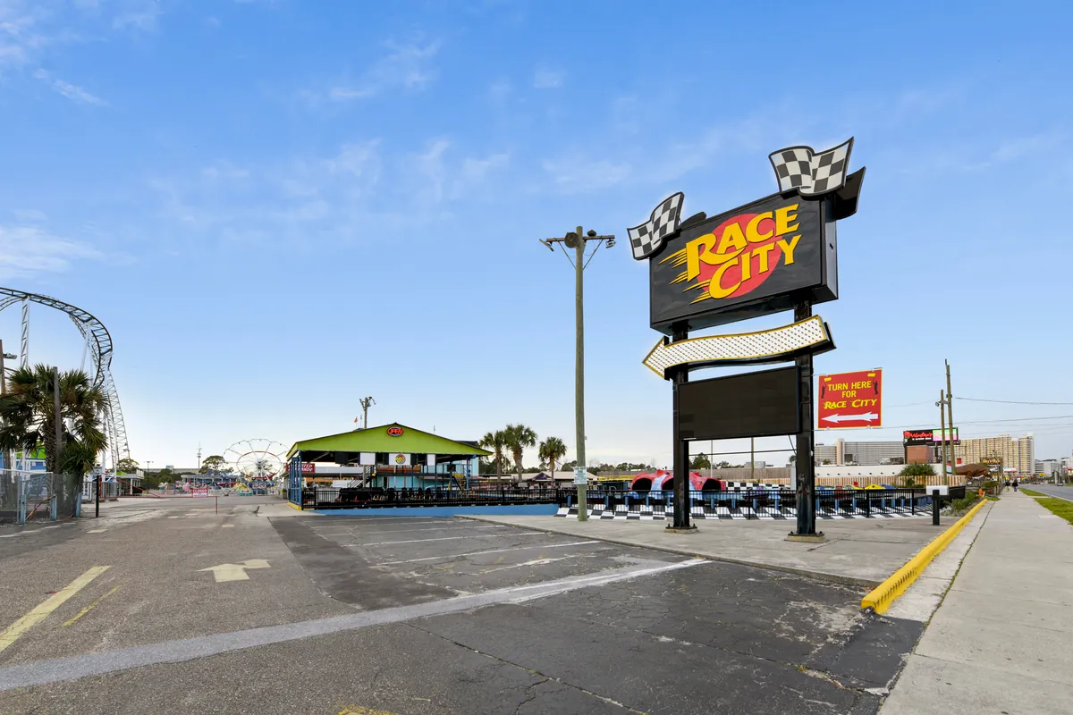 This image captures the entrance to Race City, a colorful amusement park with a prominent go-kart track and various rides visible in the background. The vibrant signage and energetic atmosphere immediately suggest fun group adventures and memorable outings.