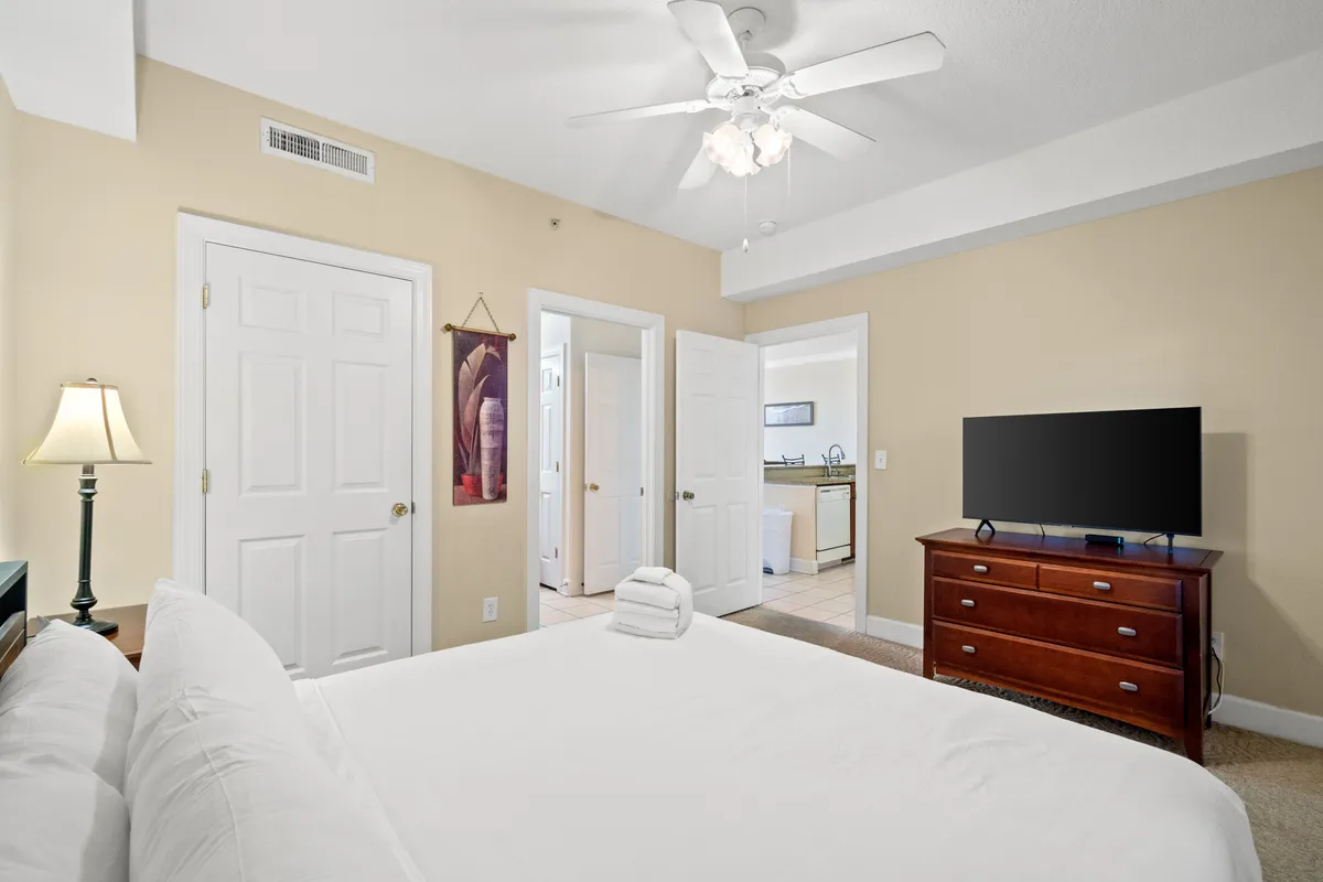 A restful second bedroom with a neatly made bed featuring crisp white linens, a wooden dresser, a lamp, and tasteful artwork on the wall. The decor is understated yet elegant, creating a soothing environment ideal for guests or family members.