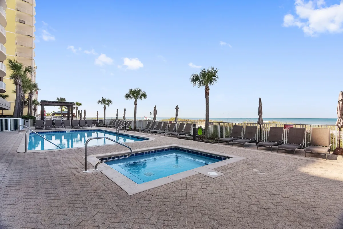 A tranquil pool area with a sparkling swimming pool, hot tub, palm trees, and a sweeping view of the ocean in the background. The scene exudes relaxation and invites families to unwind after a day of exploring local attractions.