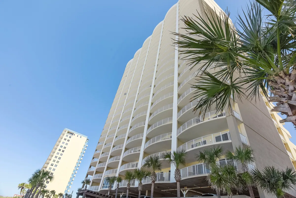 This image showcases a tall, modern condominium tower with expansive balconies and palm trees at its base, set against a clear blue sky. The architecture exudes upscale coastal living, suggesting unobstructed ocean views and the perfect setting for romantic evenings on the balcony.