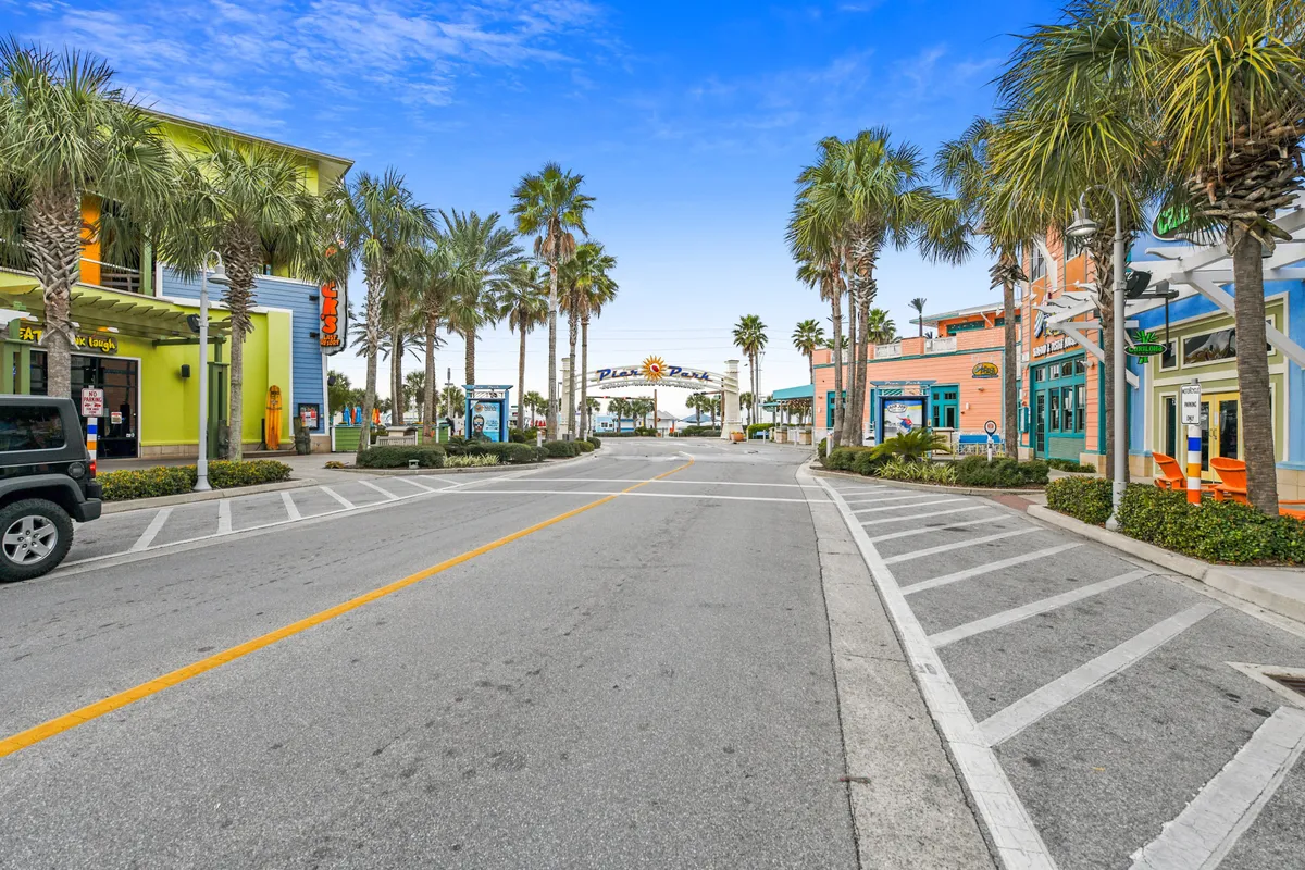 A lively street scene lined with palm trees and colorful buildings, leading to the iconic Pier Park archway. The avenue is vibrant, filled with shopping and dining venues—an inviting hub just steps from the beach.